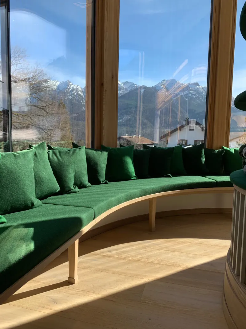 Geschwungene Sitzbank mit grünem Lodenstoff und Alpenpanorama